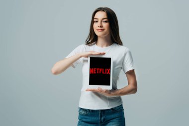 Kiev, Ukrayna - 6 Haziran 2019: Gri üzerinde izole Netflix uygulaması ile dijital tablet gösteren beyaz t-shirt gülümseyen güzel kız