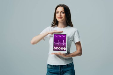gri izole sağlık uygulaması ile dijital tablet gösteren beyaz t-shirt gülümseyen güzel kız
