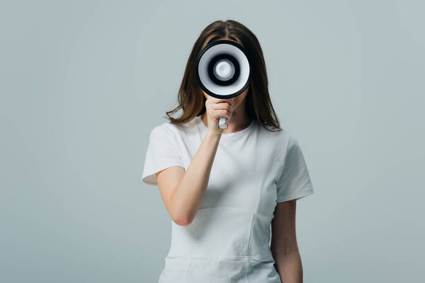 young pretty woman holding loudspeaker in front of face isolated on grey