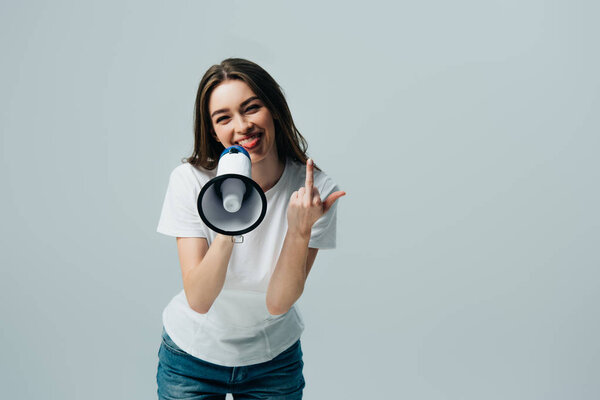 happy young pretty woman with loudspeaker showing middle finger isolated on grey