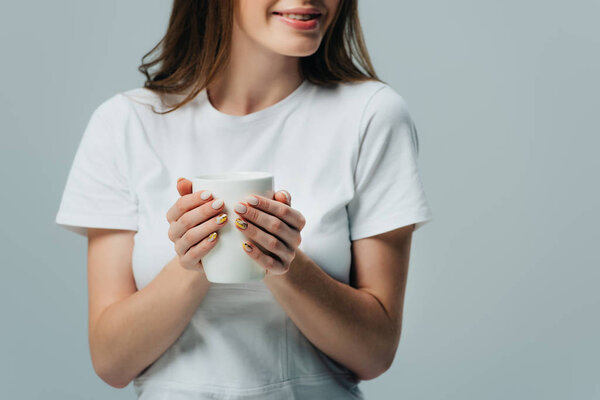 cropped view of smiling girl in white t-shirt holding white mug isolated on grey