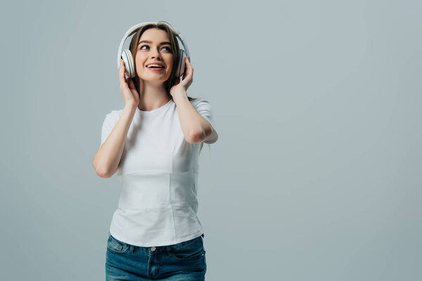 happy dreamy girl listening music in wireless headphones isolated on grey