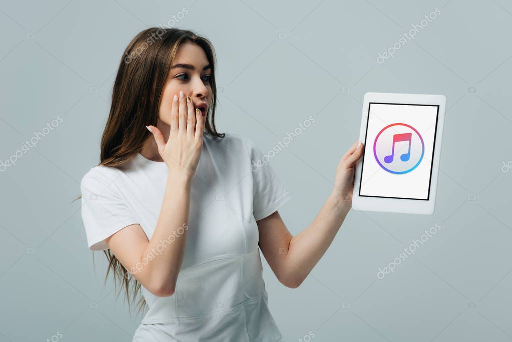 KYIV, UKRAINE - JUNE 6, 2019: shocked beautiful girl in white t-shirt showing digital tablet with Apple Music app isolated on grey