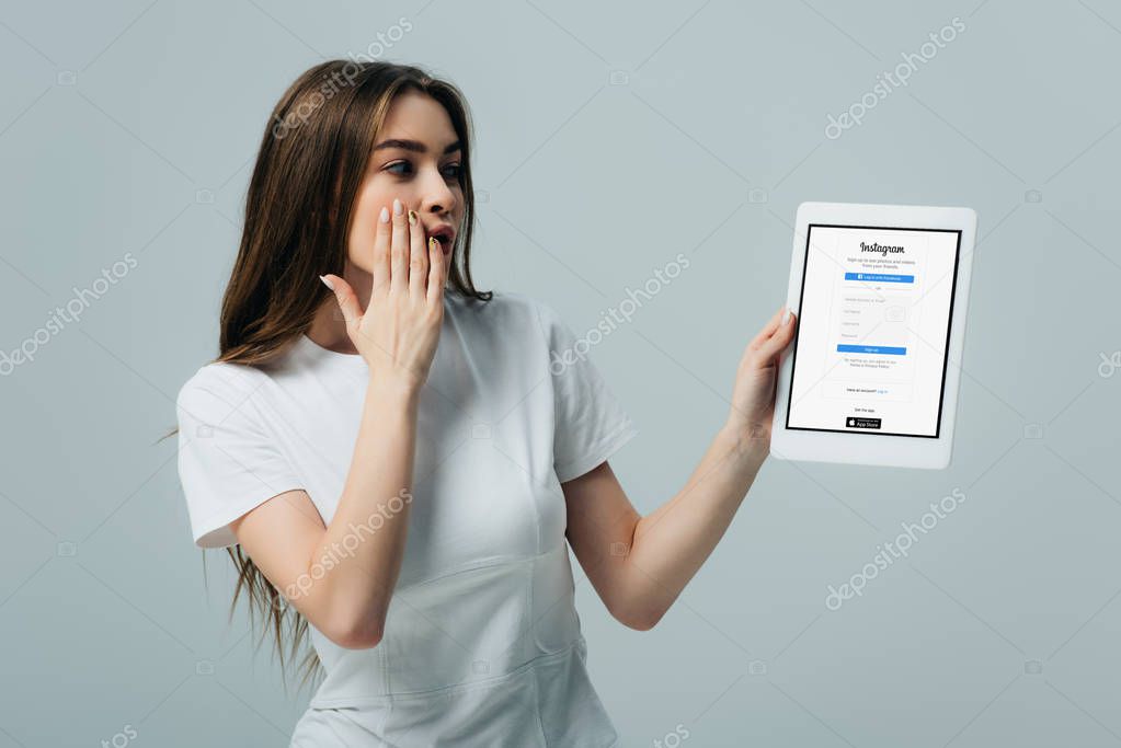 KYIV, UKRAINE - JUNE 6, 2019: shocked beautiful girl in white t-shirt showing digital tablet with Instagram app isolated on grey