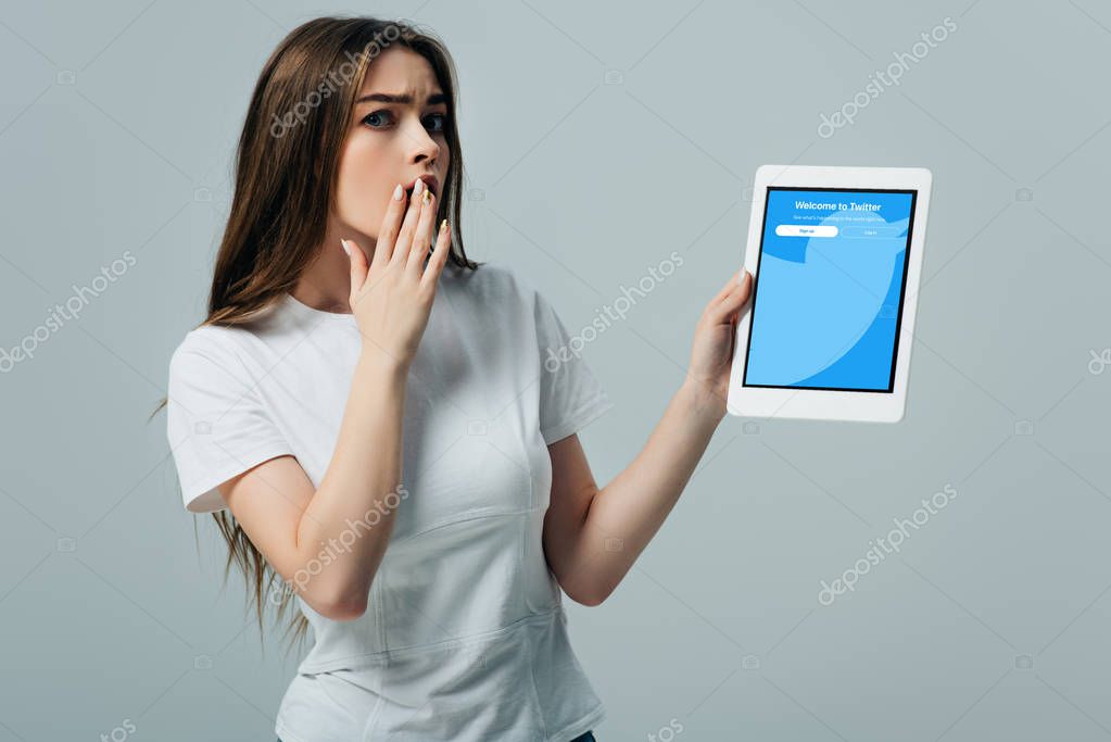 KYIV, UKRAINE - JUNE 6, 2019: shocked beautiful girl in white t-shirt showing digital tablet with twitter app isolated on grey