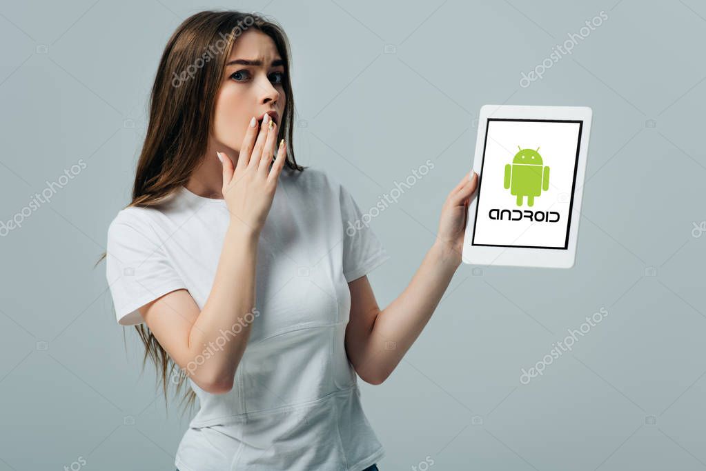 KYIV, UKRAINE - JUNE 6, 2019: shocked beautiful girl in white t-shirt showing digital tablet with android logo isolated on grey
