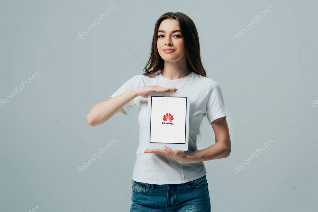 KYIV, UKRAINE - JUNE 6, 2019: smiling beautiful girl in white t-shirt showing digital tablet with Huawei isolated on grey