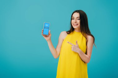 Kiev, Ukrayna - 6 Haziran 2019: turkuaz üzerinde izole Skype uygulaması ile akıllı telefon parmak ile işaret sarı elbiseli mutlu güzel kız