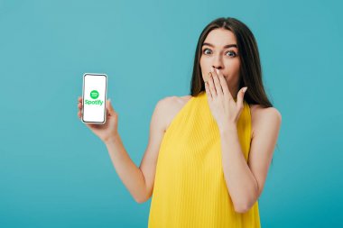 Kiev, Ukrayna - 6 Haziran 2019: turkuaz üzerinde izole spotify uygulaması ile akıllı telefon gösteren sarı elbiseli güzel kız şok