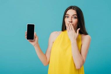 turkuaz izole boş ekran ile akıllı telefon gösteren sarı elbiseli şok güzel kız