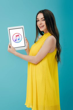 Kiev, Ukrayna - 6 Haziran 2019: turkuaz üzerinde izole itunes uygulaması ile dijital tablet gösteren sarı elbiseli güzel kız gülümseyen