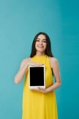 turkuaz izole boş ekran ile dijital tablet gösteren sarı elbiseli gülümseyen esmer kız