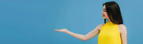 Щаслива Красива Дівчина Жовтій Сукні Вказуючи Рукою Сторону Ізольована Синьому — стокове фото