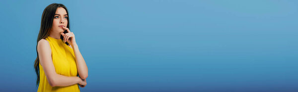 мечтательная красивая девушка в желтом платье глядя в сторону изолированы на синий, панорамный снимок
