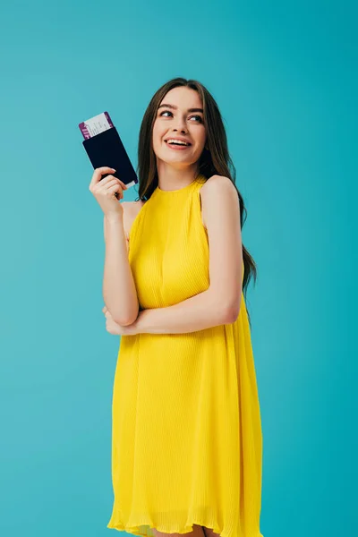 ターコイズに隔離された航空券でパスポートを保持する黄色のドレスを着た幸せなブルネットの女性 — ストック写真