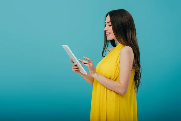 侧视图微笑的漂亮女孩在黄色礼服使用数字平板电脑在绿松石背景 — 图库照片