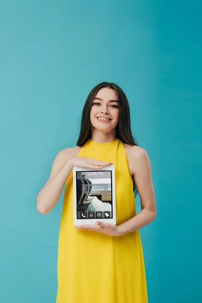 ターコイズに隔離されたチケットアプリでデジタルタブレットを示す黄色のドレスで美しいブルネットの女の子 — ストック写真