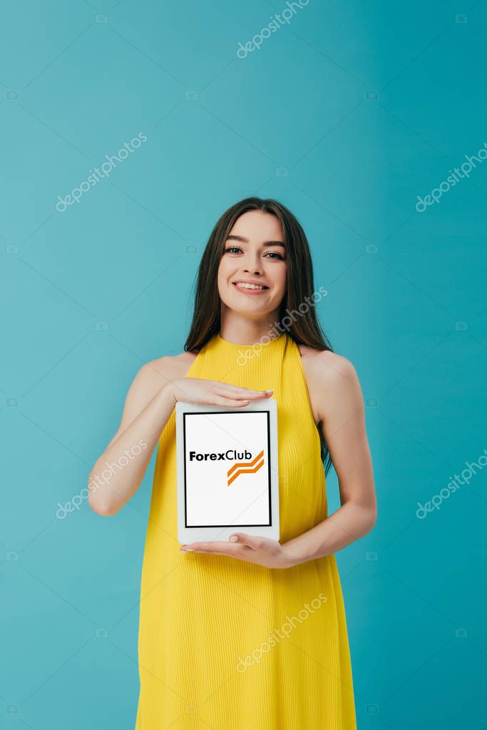 KYIV, UKRAINE - JUNE 6, 2019: smiling beautiful girl in yellow dress showing digital tablet with forex club app isolated on turquoise