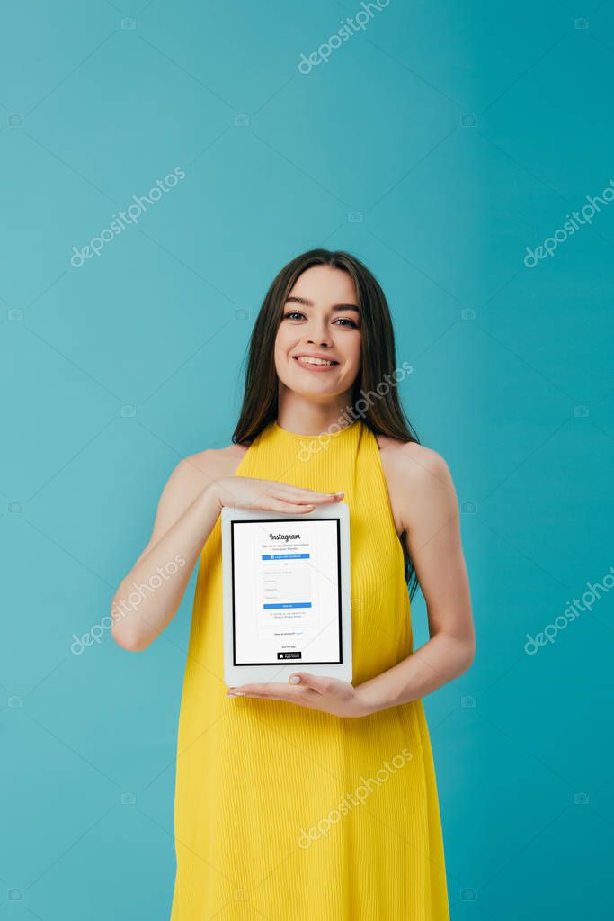 KYIV, UKRAINE - JUNE 6, 2019: happy beautiful girl in yellow dress showing digital tablet with instagram app isolated on turquoise