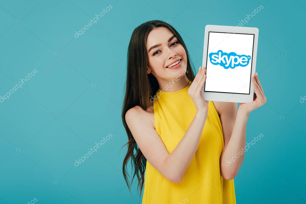 KYIV, UKRAINE - JUNE 6, 2019: happy beautiful girl in yellow dress showing digital tablet with skype app isolated on turquoise