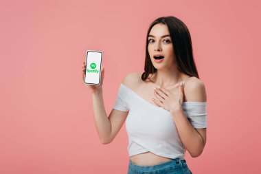 Kiev, Ukrayna - 6 Haziran 2019: Pembe izole Spotify uygulaması ile akıllı telefon tutan güzel şok kız