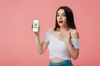 Kiev, Ukrayna - Haziran 6, 2019: güzel şok kız pembe izole Android logosu ile akıllı telefon tutan