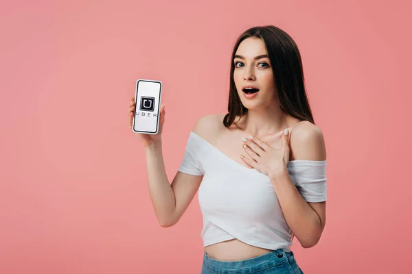 乌克兰 2019年6月6日 美丽的震惊的女孩拿着智能手机与优步应用程序隔离在粉红色 — 图库照片