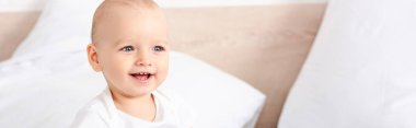 Panoramic shot of cute little child with blue eyes smiling in white room clipart