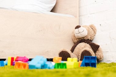 Peluş ayı ve ahşap yatak yakınında yeşil halı üzerinde inşaat dağınık parçaları
