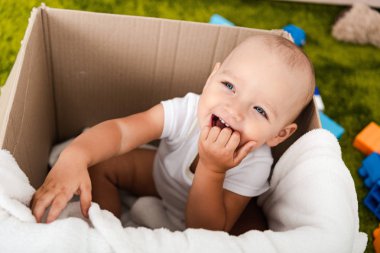 Sevimli mavi gözlü çocuk oturan ve battaniye ile karton kutu içinde gülümseyen