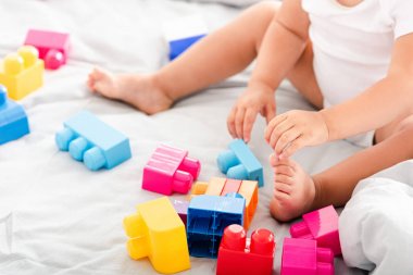 Yatakta oturan ve parlak inşaat ile oynarken beyaz giysiler içinde yalınayak bebek Kısmi görünümü