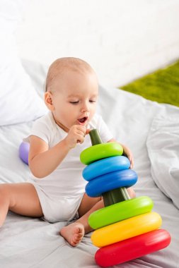 oyuncak piramidi ile yatakta oturan beyaz giysiler içinde sevimli yalınayak çocuk 
