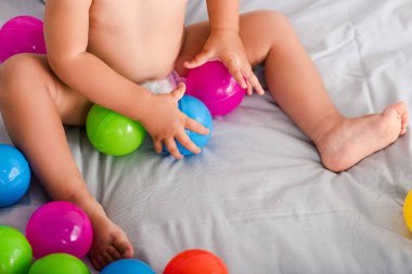 Küçük ellerle renkli topları kapma yatakta sevimli küçük bebek Kırpılmış görünümü