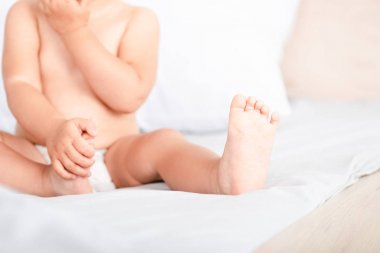 Beyaz yatakta oturan küçük ayak parmakları ve parmakları ile küçük çocuğun Kısmi görünümü