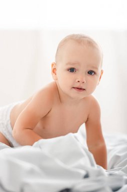 Sevimli küçük çocuk beyaz kumaş üzerinde sürünen ve kamera bakarak