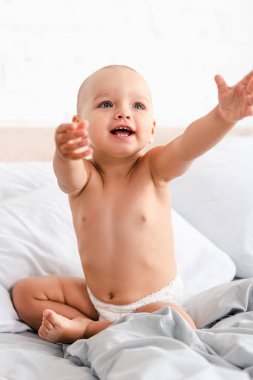 Bebek bezi içinde sevimli küçük çocuk gülümseyerek ve ellerini yukarı kaldırarak