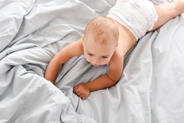 Beyaz yatak üzerinde yatan ve uzağa bakan bebek bezi sevimli bebek