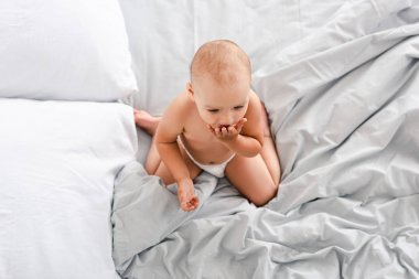 Beyaz çarşaflar üzerinde oturan ve el ile ağız kapsayan bebek üst görünümü