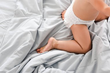 Cropped view of cute baby in diaper kneeing on white blanket clipart
