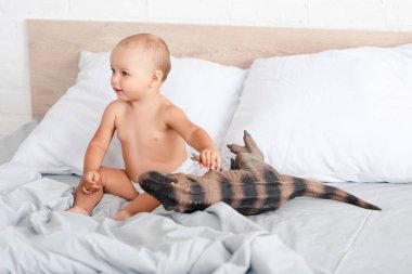 Sevimli küçük çocuk yatakta oturan ve kahverengi oyuncak dinozor tutarak