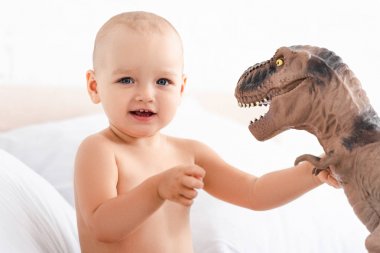 Sevimli küçük çocuk kameraya bakıyor ve kahverengi oyuncak dinozor tutarak
