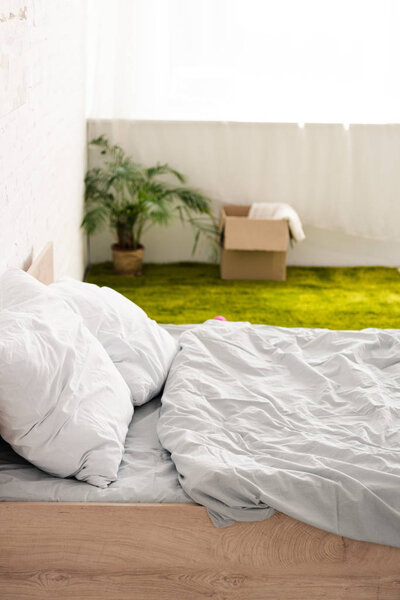 Bed with white bedclothes near green carpet with cardboard box