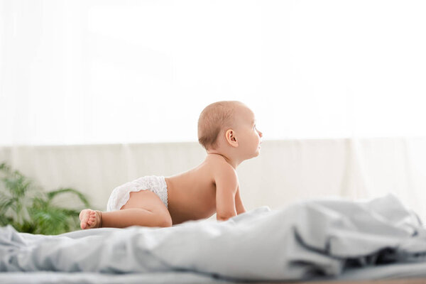 Вид сбоку симпатичного маленького ребенка, который ползает по кровати и смотрит в сторону
