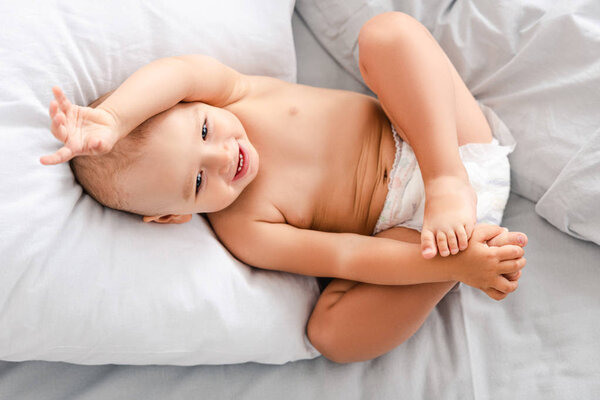 Вид сверху восхитительного младенца в пеленке, лежащего на спине и болтающего ногой
 