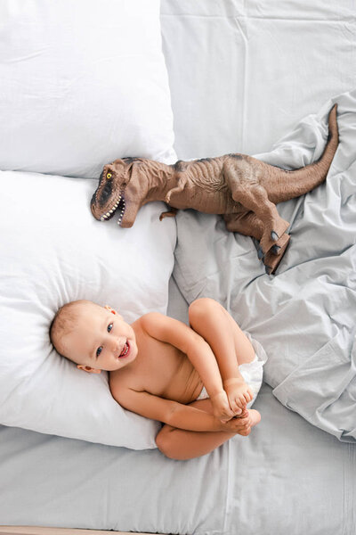 Little child laying on back near toy dinosaur and smiling