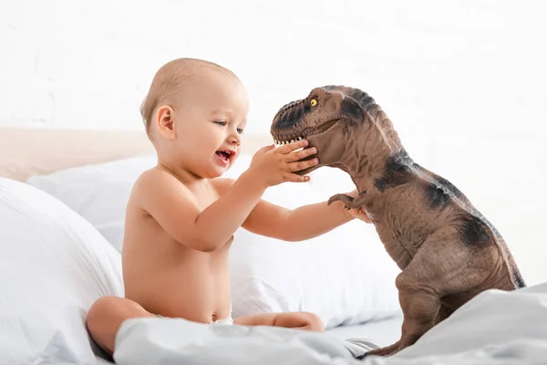 Litet Barn Sitter Vita Sängen Och Håller Leksaks Dinosaurie Med — Stockfoto