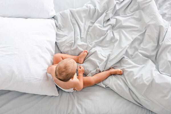 Top view of little child sitting on bed with crumpled light blanket