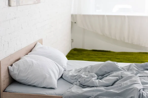 木製ベッド 枕付き 緑のカーペット付きの白い部屋にくしゃくしゃの軽い毛布 — ストック写真