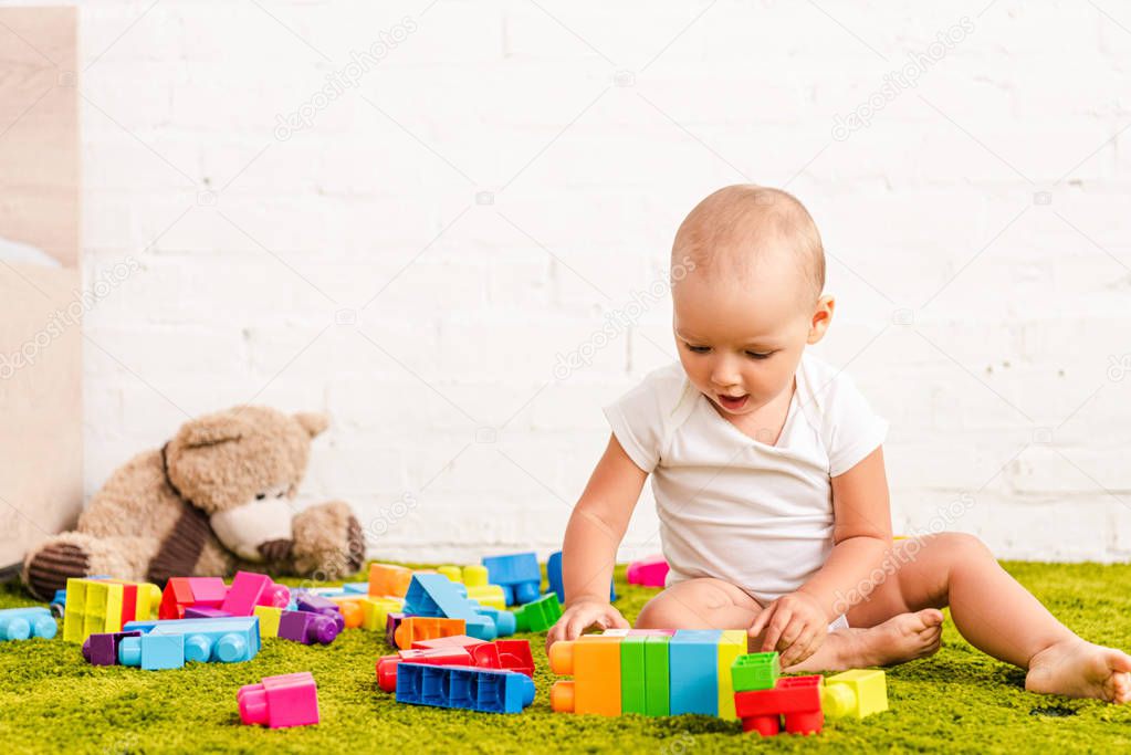 cute little child playing with colorful toys on green floor 