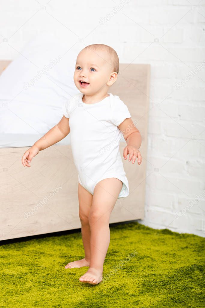 Happy little child smiling and walking through light room with bed and green carpet